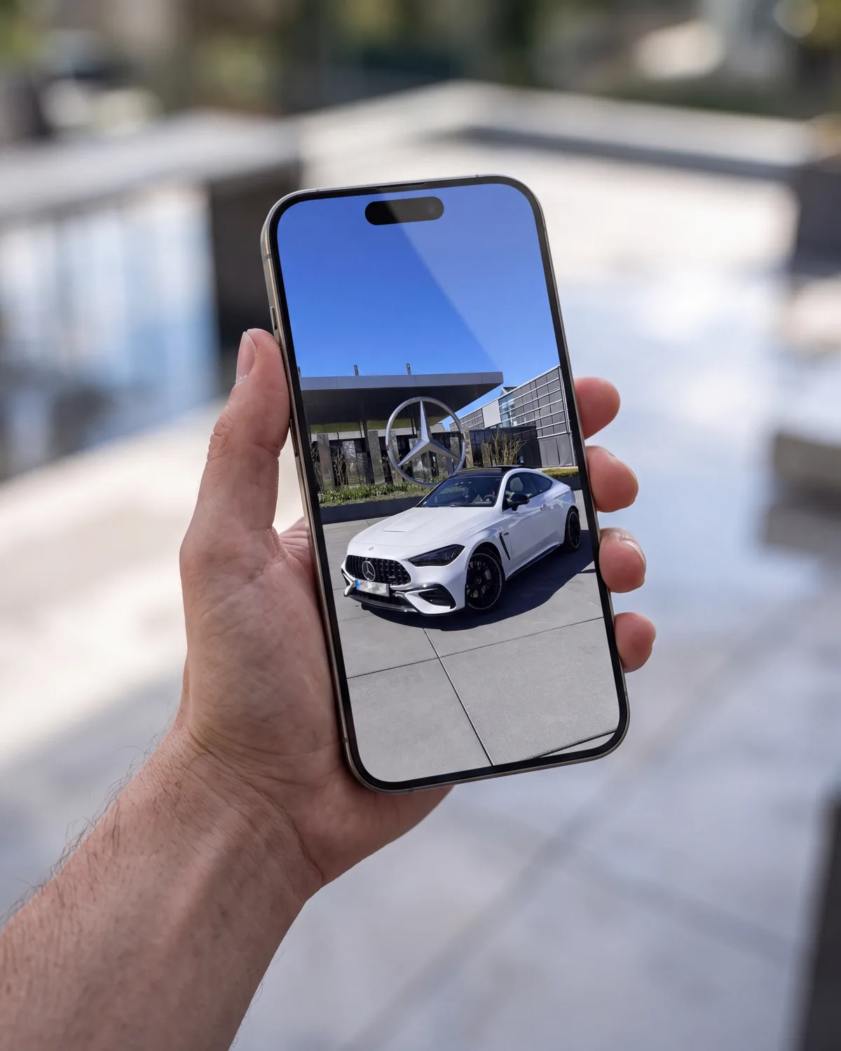 Eine Hand hält ein Smartphone, auf dem das Foto eines weißen Coupés zu sehen ist